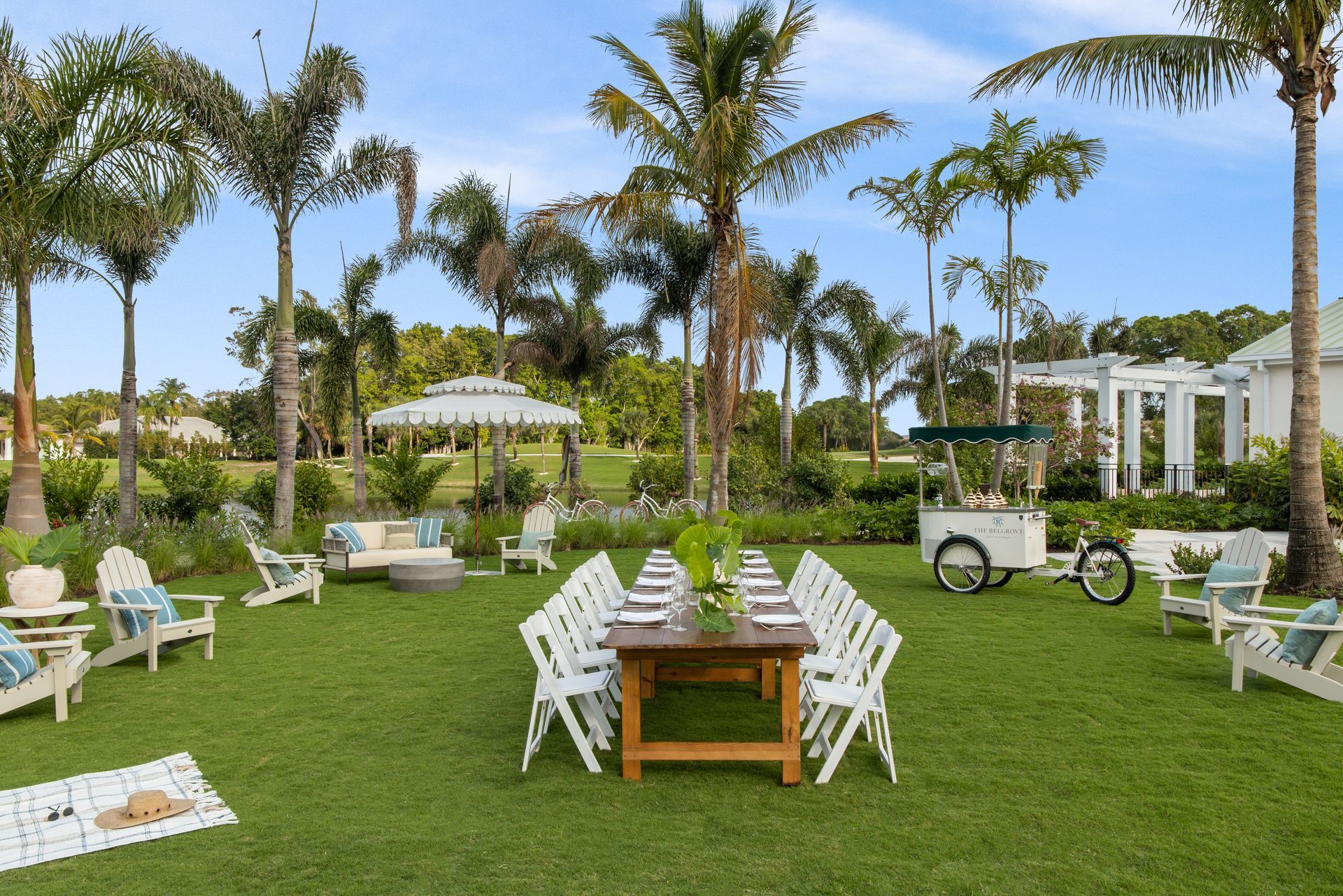 A table and chairs are set up in a lush green field surrounded by palm trees.