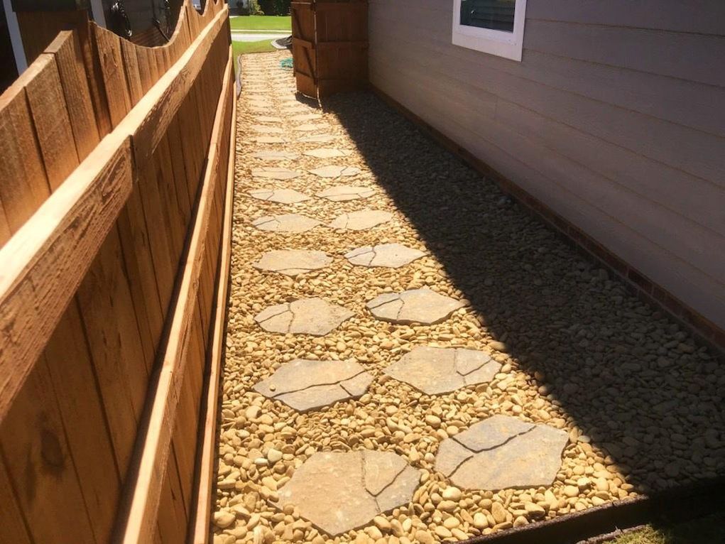 Pathway between wooden fence and building with stepping stones and gravel.