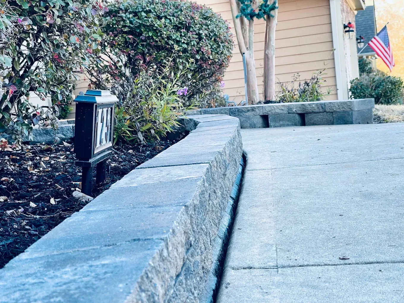 Concrete retaining wall borders a sidewalk and dark mulch bed with shrubs.
