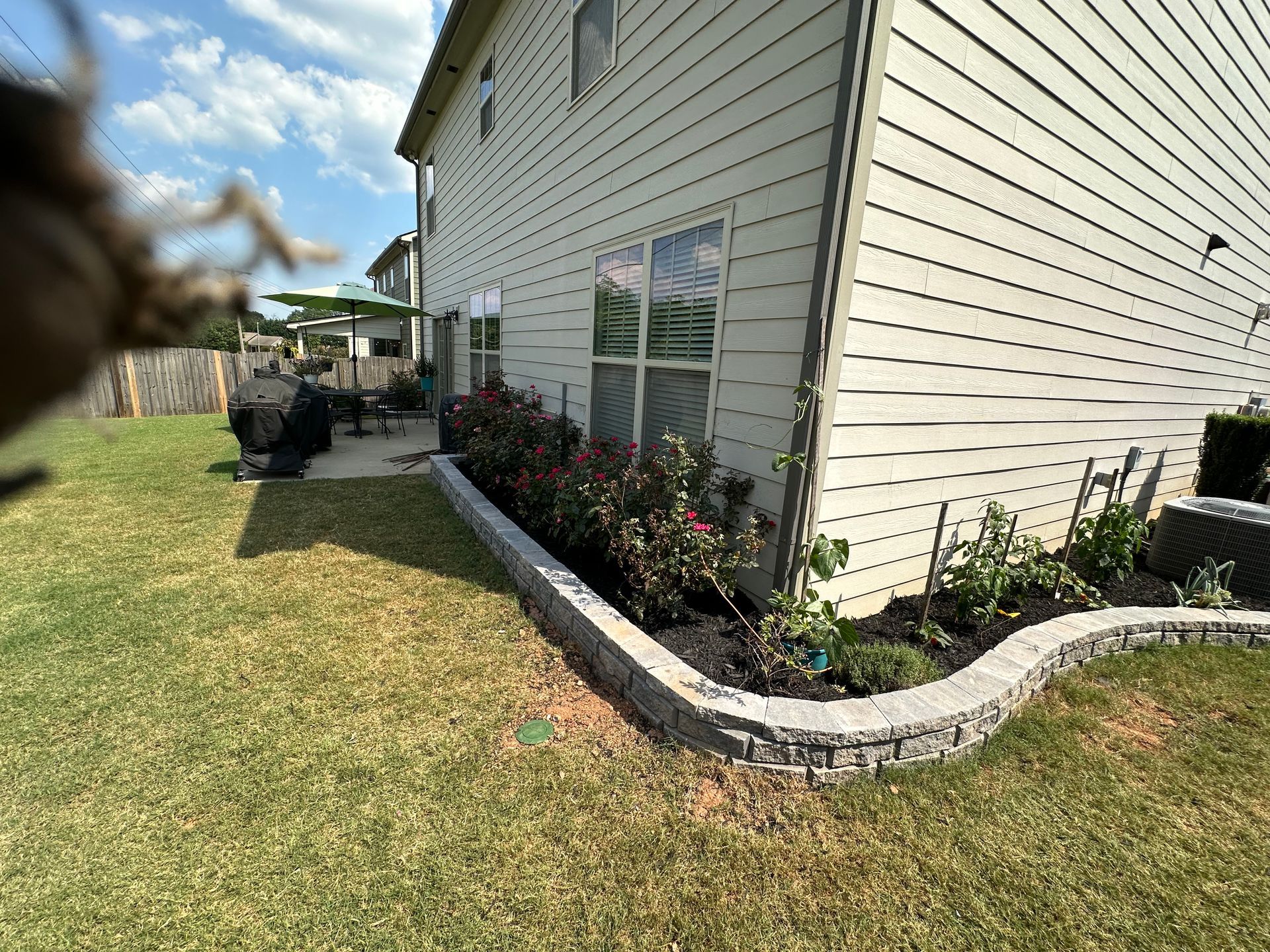 Stone steps and retaining wall leading to a grassy yard with trees, a fire pit, and a small yellow tractor.