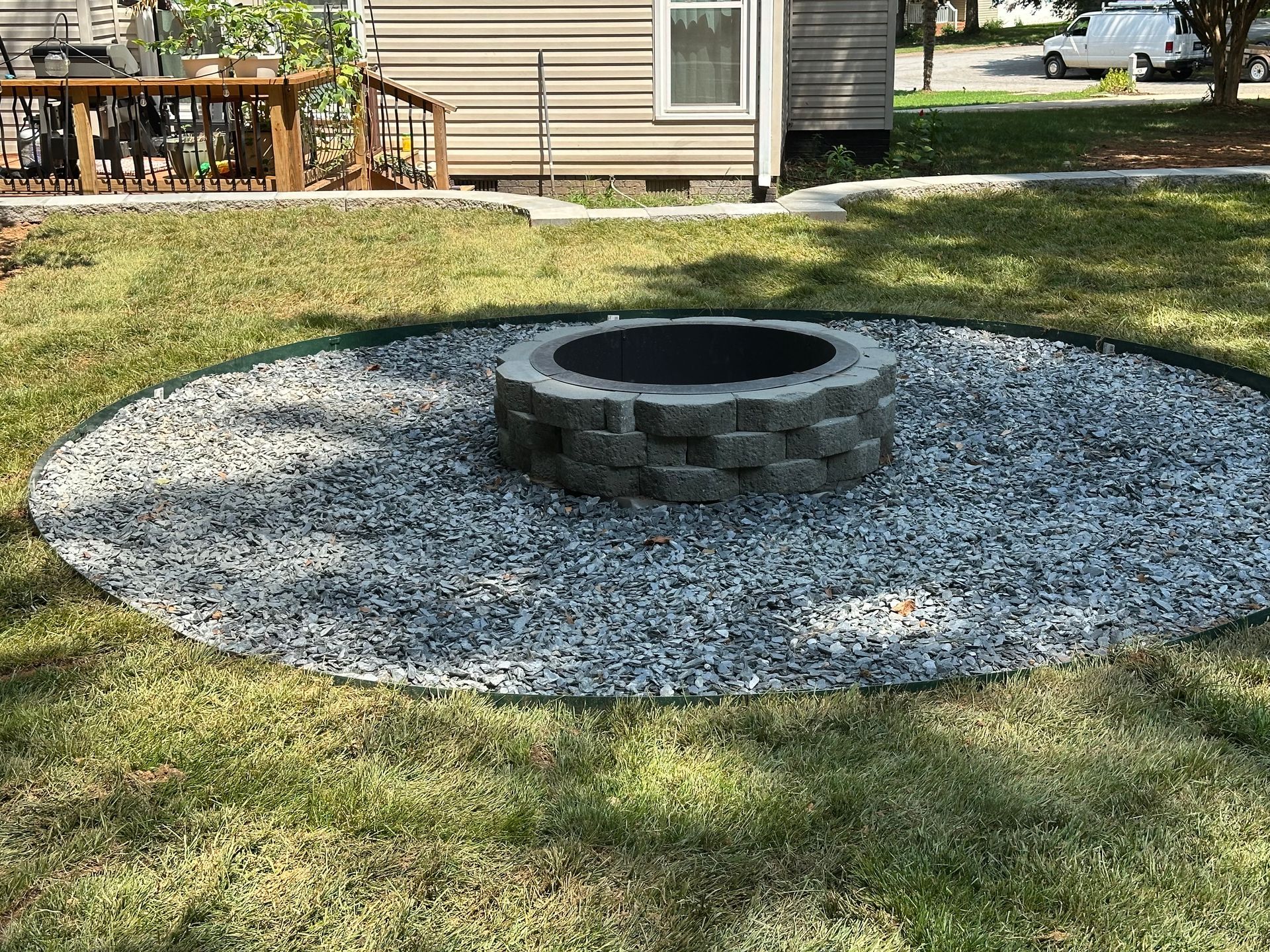Fire pit surrounded by gravel, on grass lawn. House and deck in background.