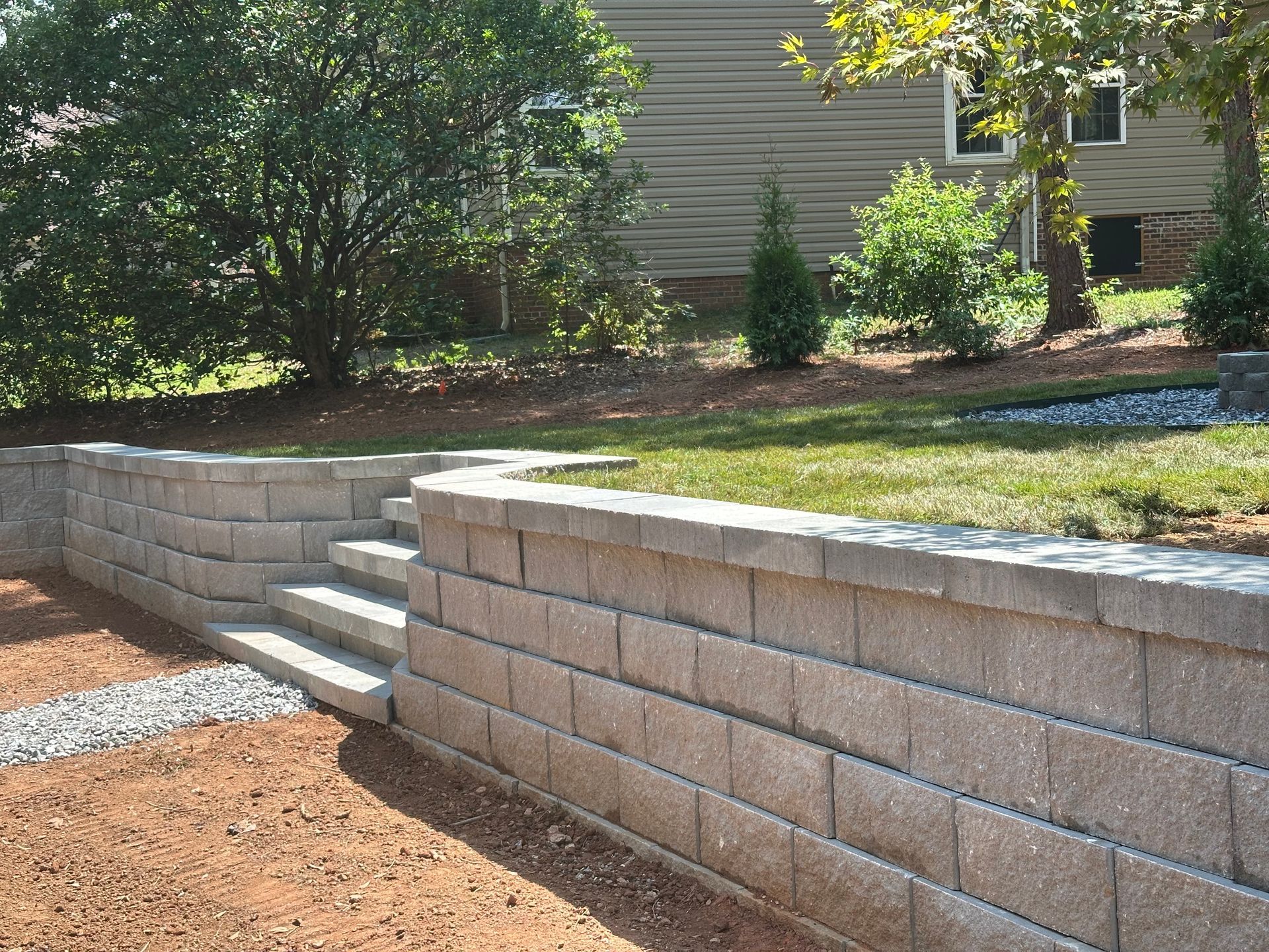 Stone retaining wall with steps leading up to a grassy area, a house visible in the background.