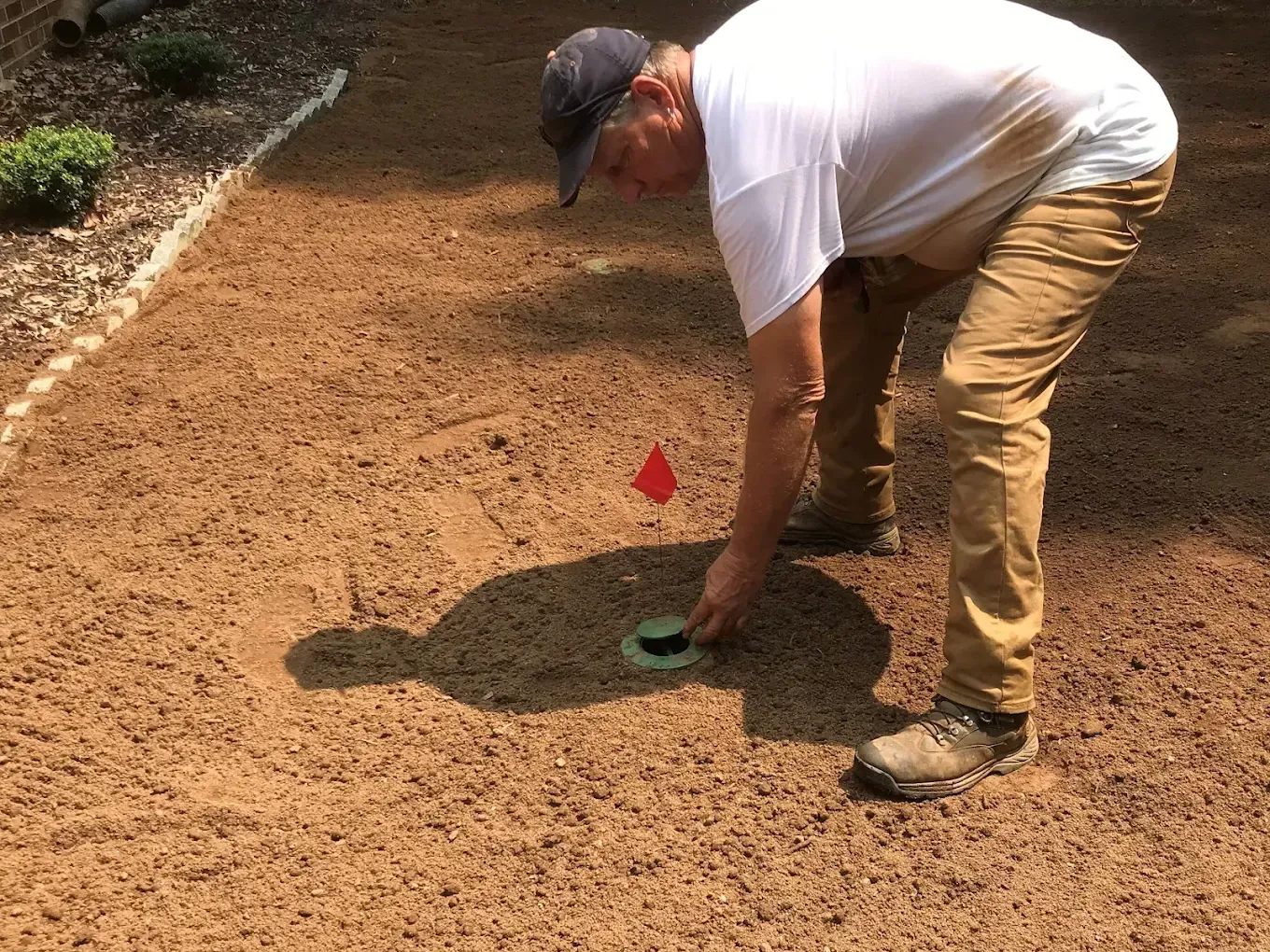 Man placing something in a golf hole, on a sandy surface. Red flag visible.