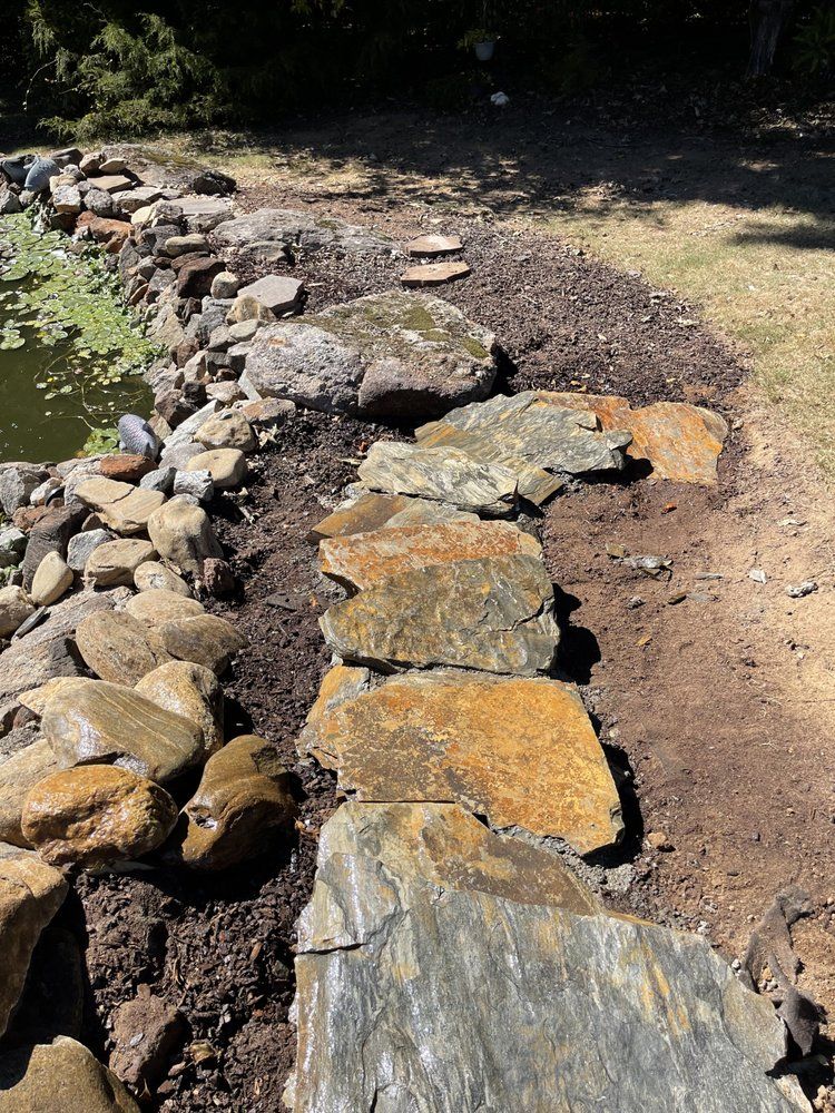 Stone pathway and pond edging made of large rocks in an outdoor setting with mulch.