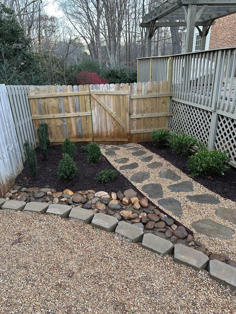 Pathway of stones through a backyard garden, with a wooden fence and gate.