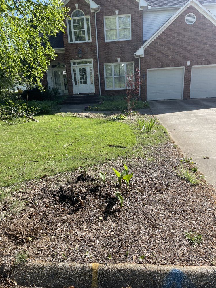 Front view of a two-story brick house with a lawn and driveway. A garden bed is in the foreground.