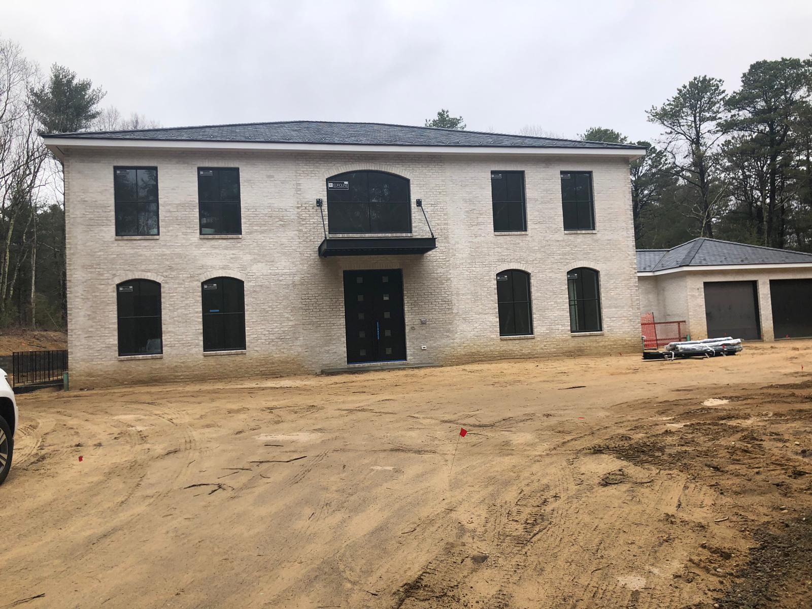 Two-story brick house with black windows and doors under construction; sand in front.