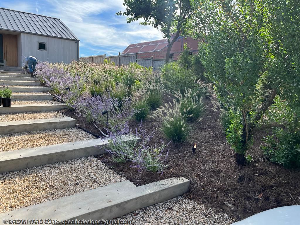 Concrete steps lead up to a garden bed with purple flowers and a shed in the background.