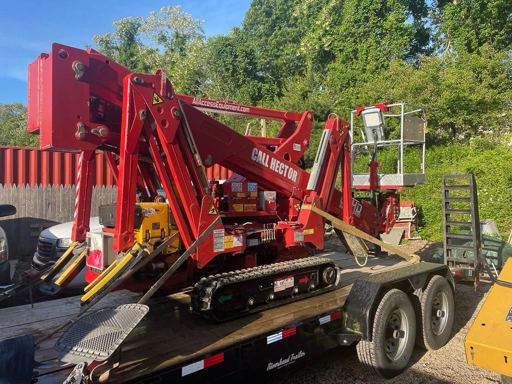 Red tree trimming machine on a trailer, next to a person in a lift.