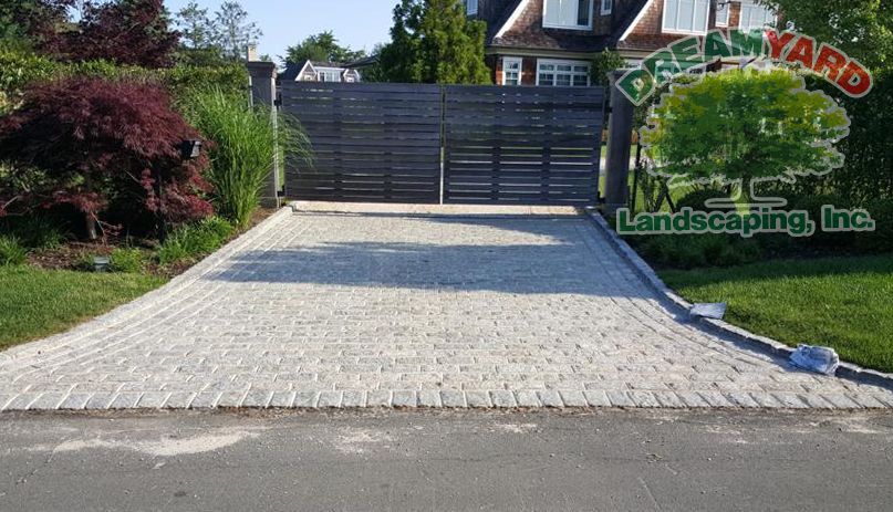 A paved driveway with a dark wooden gate, leading to a house, and DreamYard Landscaping logo.