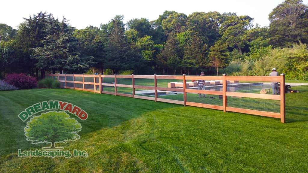 Wooden fence in a green yard with trees in the background, Dream Yard Landscaping logo on the left.