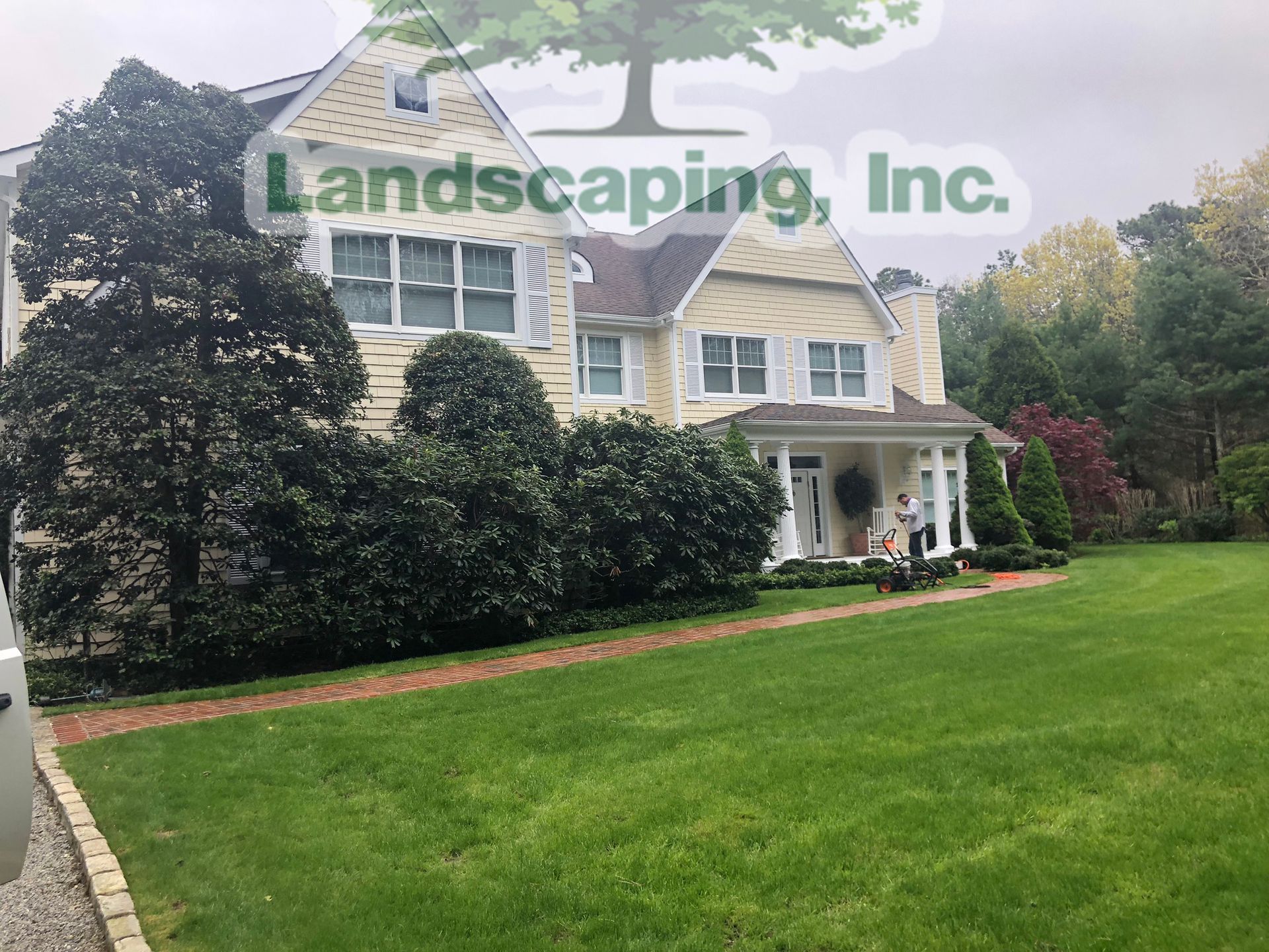 Yellow house with lush green lawn, bushes, and trees.