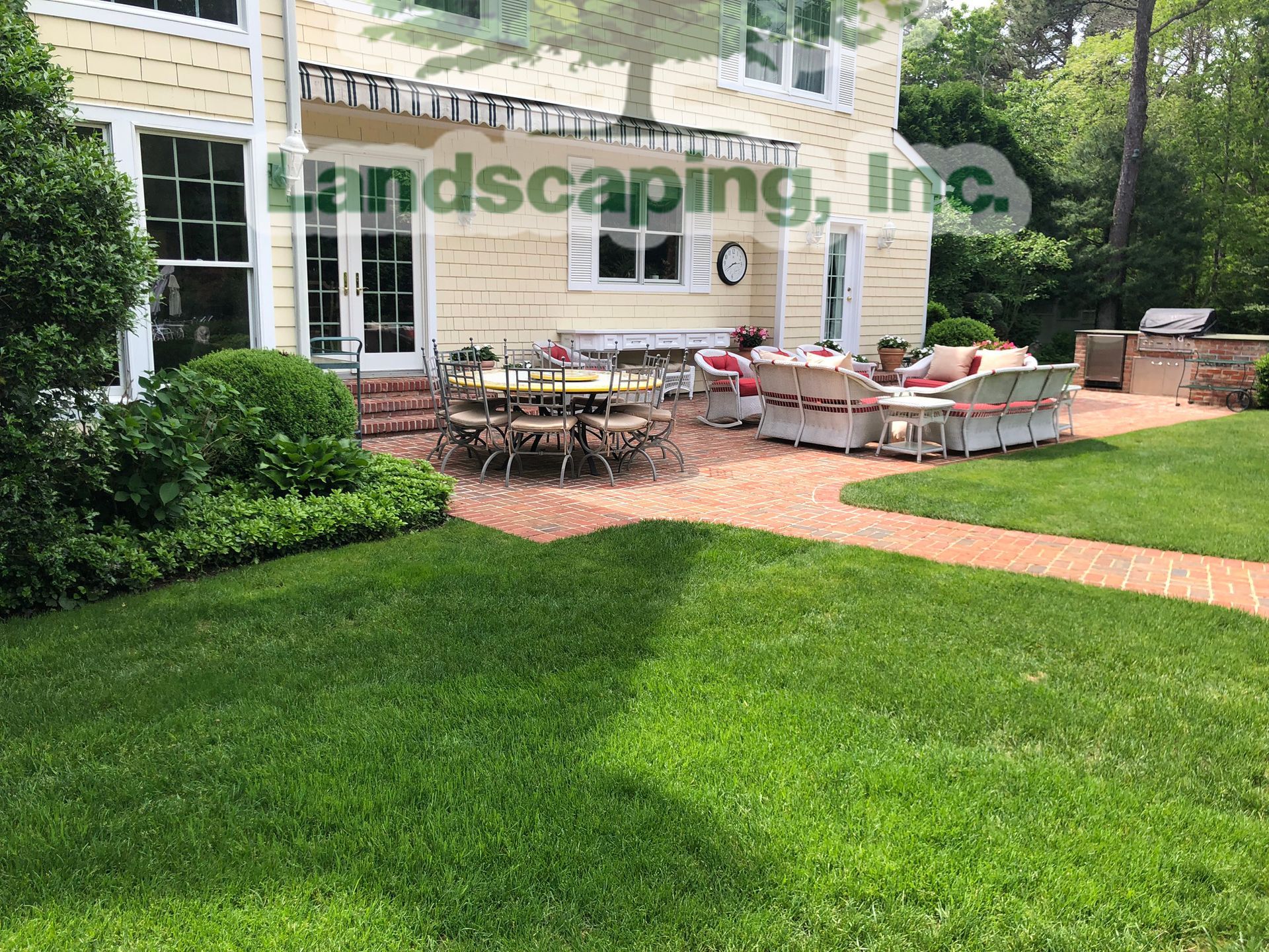 A brick patio with outdoor furniture, a grassy lawn, and a yellow house.