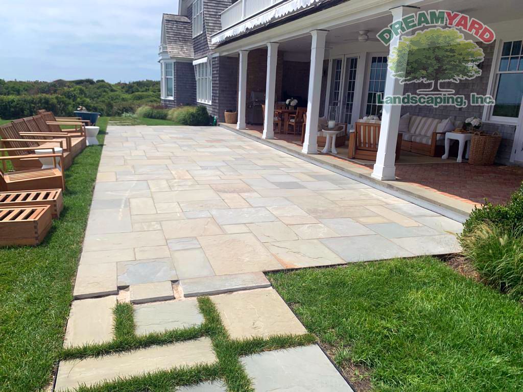 Patio with stone pavers, grass, and a porch, possibly for a home.