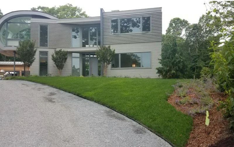 Modern house with curved glass section, two stories, gray siding, and manicured lawn.