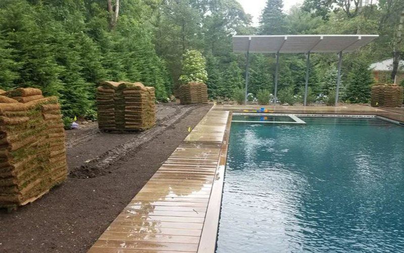 Stacks of sod next to a pool, with a modern roof structure in the background.