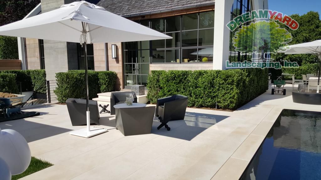 Patio with seating, umbrella, and pool. Green hedges frame the modern outdoor space.