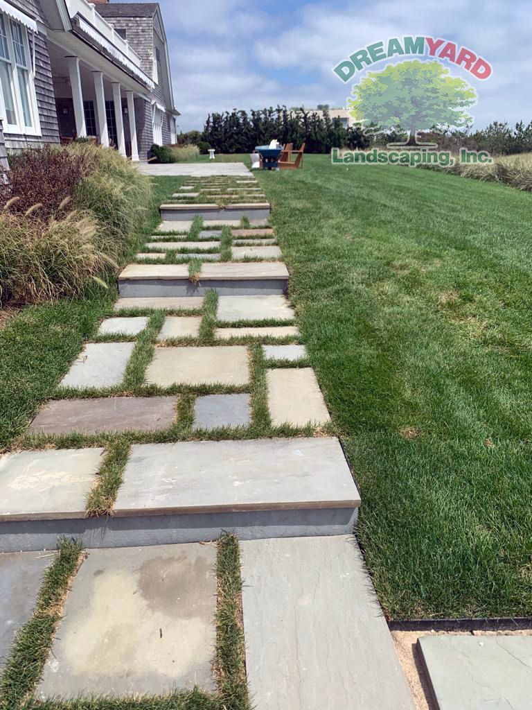 Stone walkway with grass borders leads to house; sunny day.