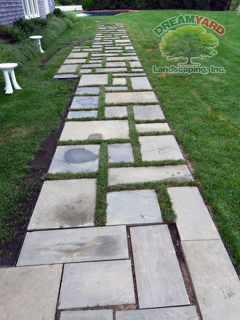Stone pathway with grass between pavers in a green lawn.