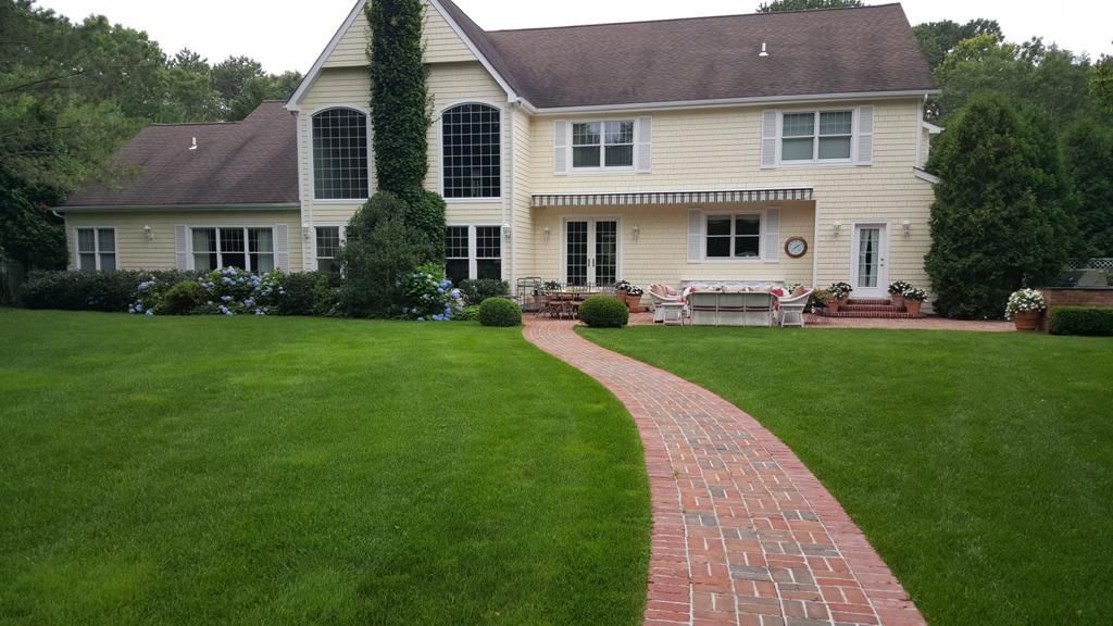 Yellow house with red brick path through green lawn.