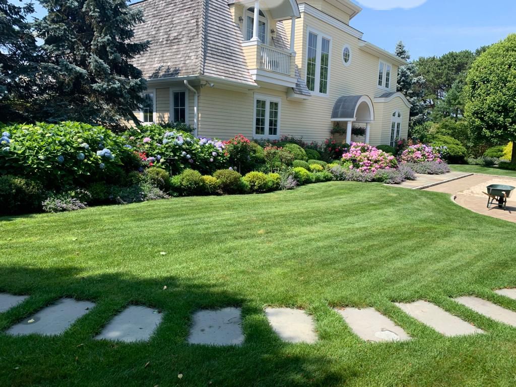 Yellow house with manicured lawn, stone walkway, and colorful flower beds.