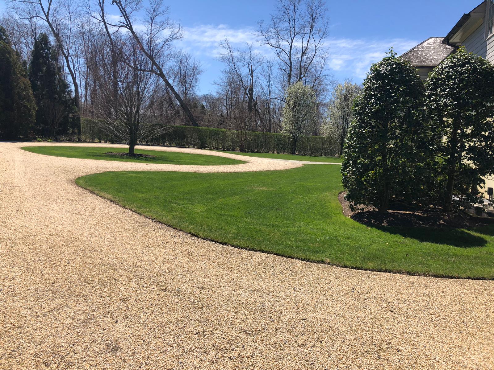 Curving gravel driveway beside a green lawn, trees in the background under a clear blue sky.