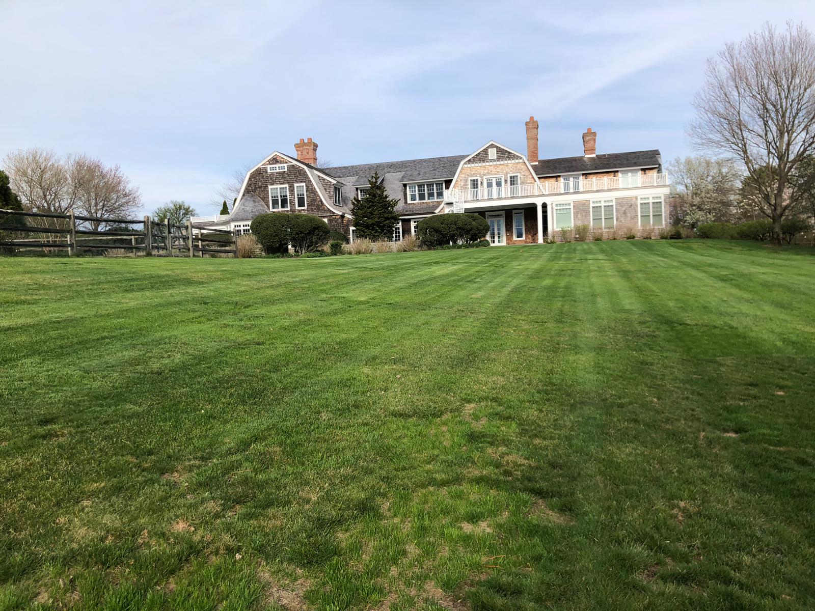Large house with shingled roof on a grassy hill; green lawn, blue sky.
