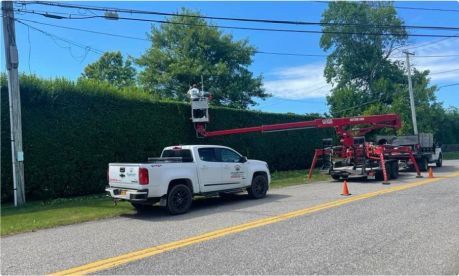 Truck with lift trimming tall hedge near power lines.
