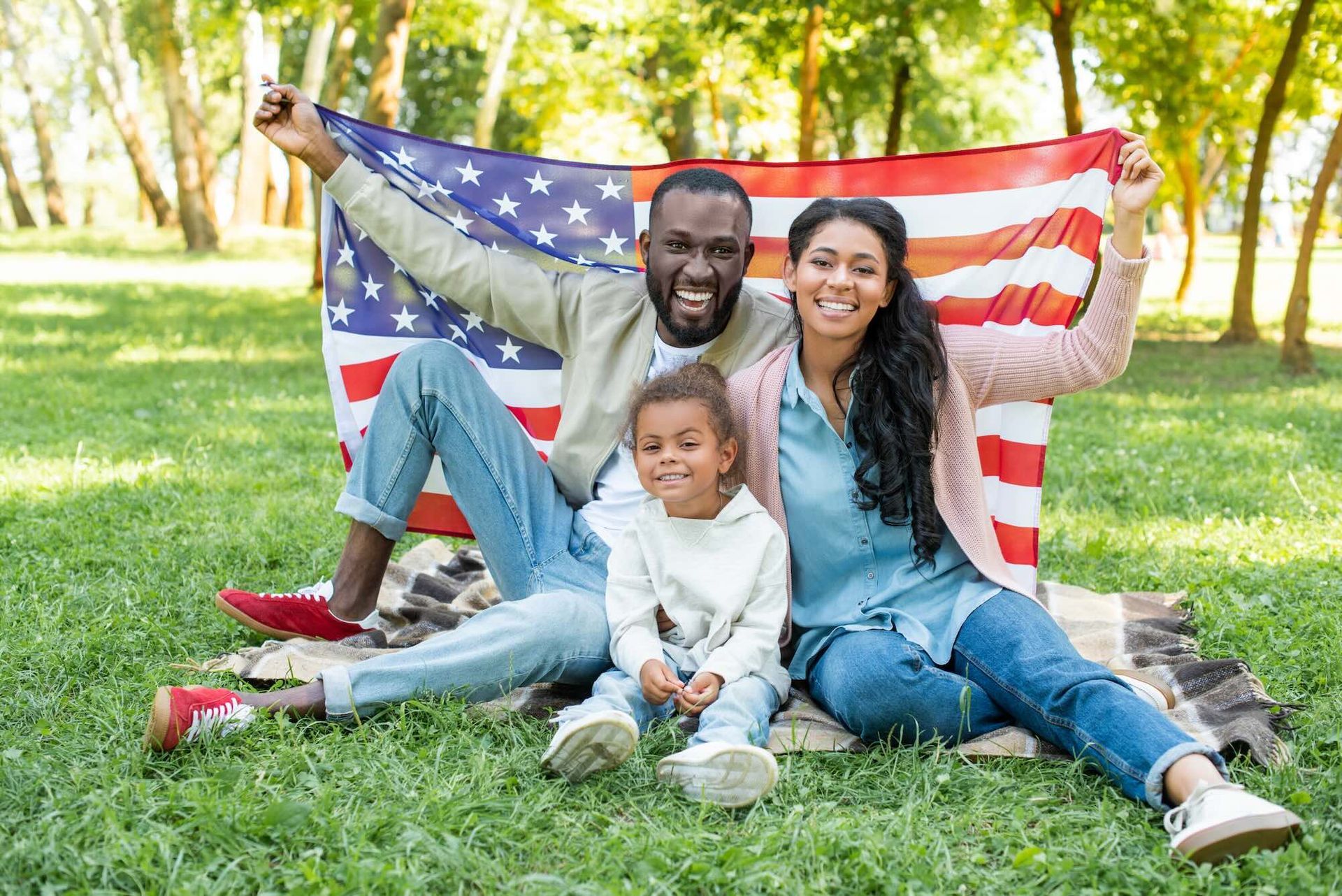 Family with US flag, sitting on grass, smiling.