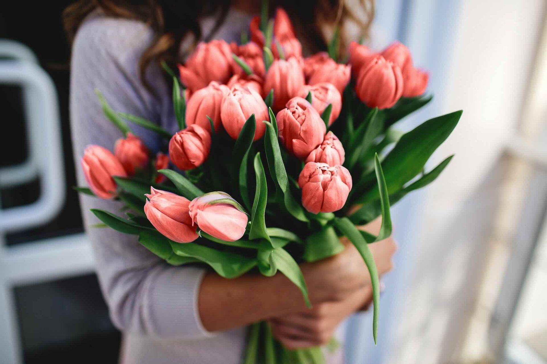 Woman holding a bouquet of coral-colored tulips, blurred background.