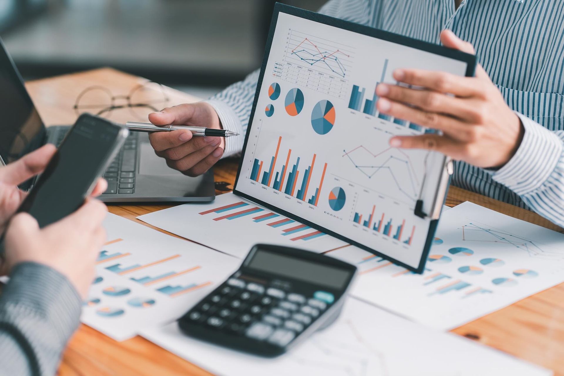 Two people reviewing financial charts and data with calculator and phone at a desk.