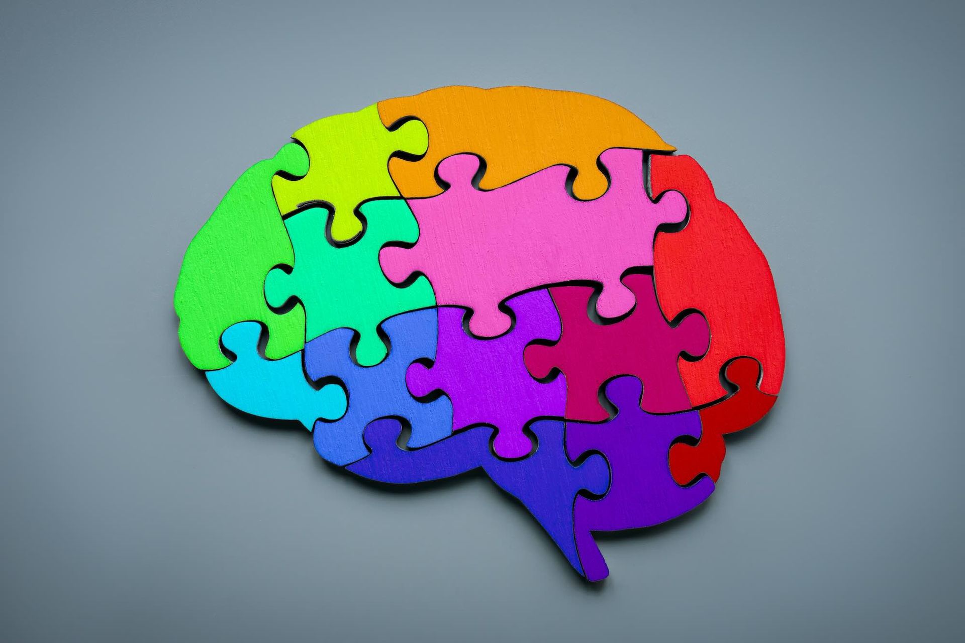 A colorful jigsaw puzzle in the shape of a brain, with different colored pieces, on a gray background.