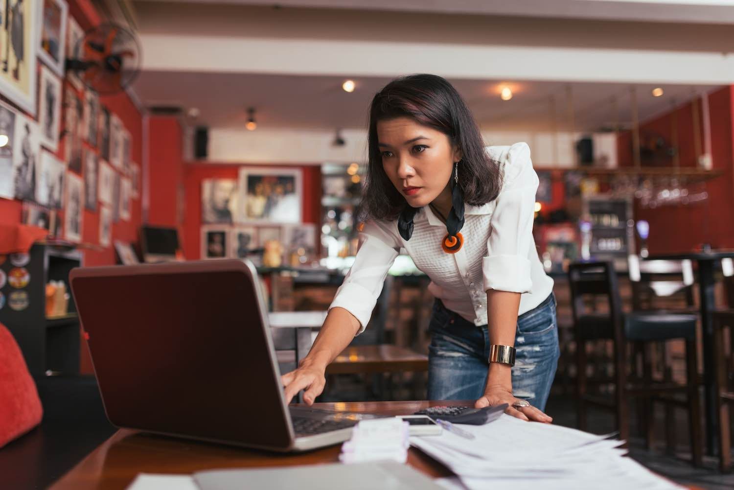 Woman working intently on a laptop at a table in a restaurant.