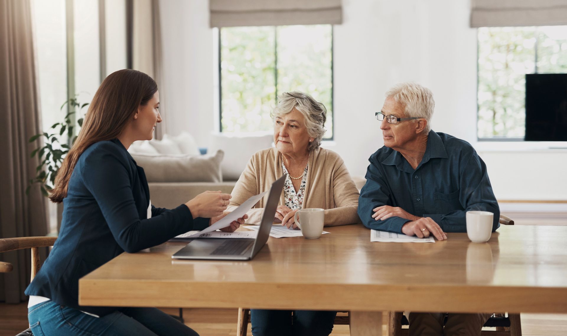 Woman advises elderly couple, discussing paperwork at a table in a home.