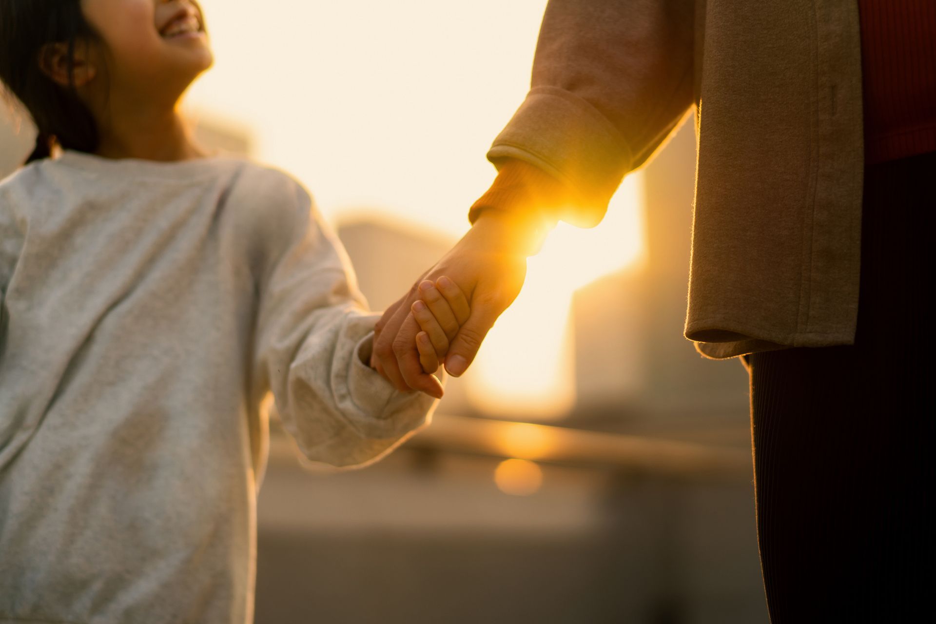 A child smiling, holding hands with an adult, sunset in the background.