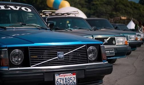 Blue vintage Volvo cars lined up on a street, front car in focus with California plate.