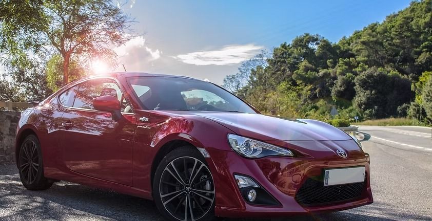 Red sports coupe driving on a sunny road with trees and blue sky