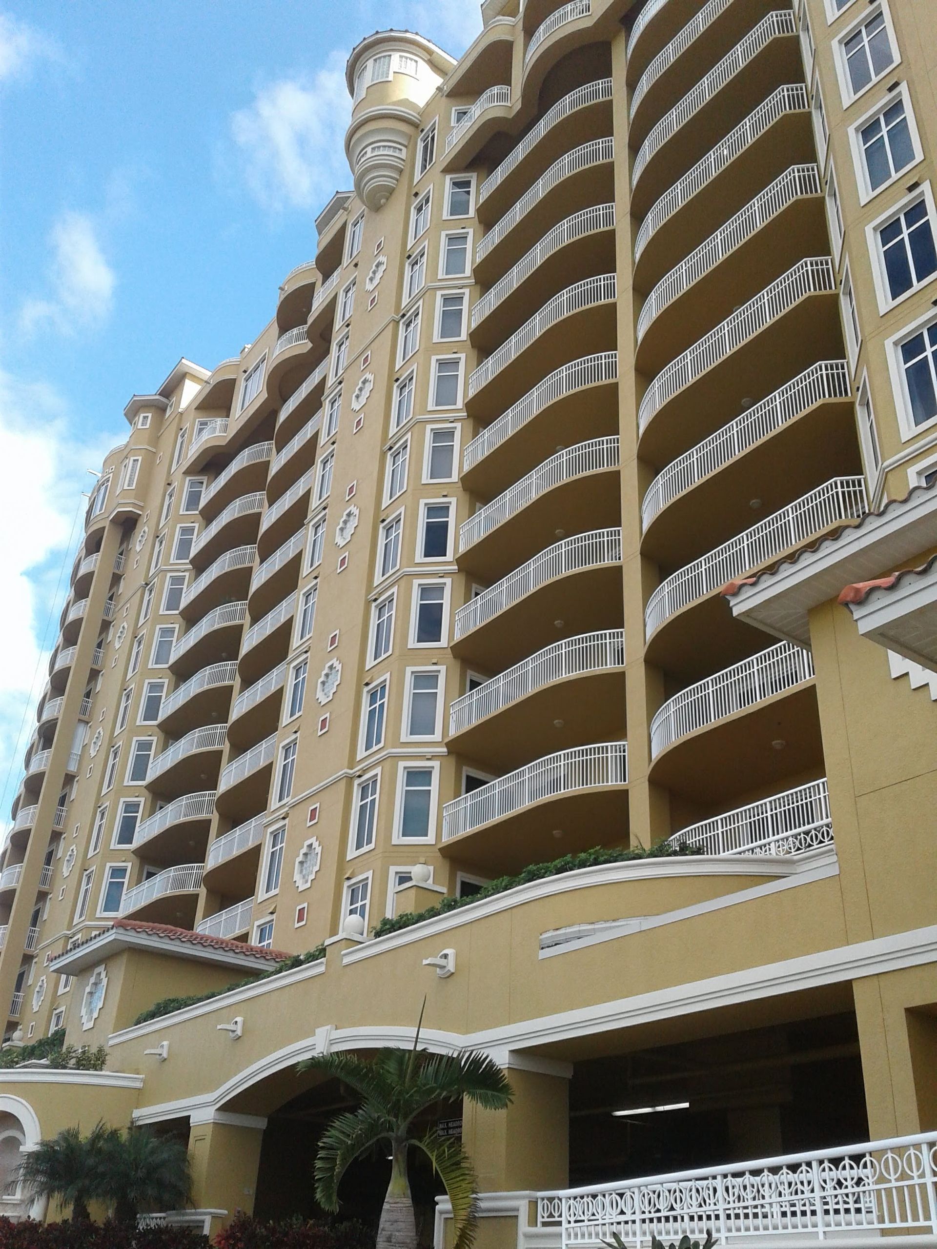 Wooden deck with above-ground pool and pergola, surrounded by houses and trees on a sunny day.