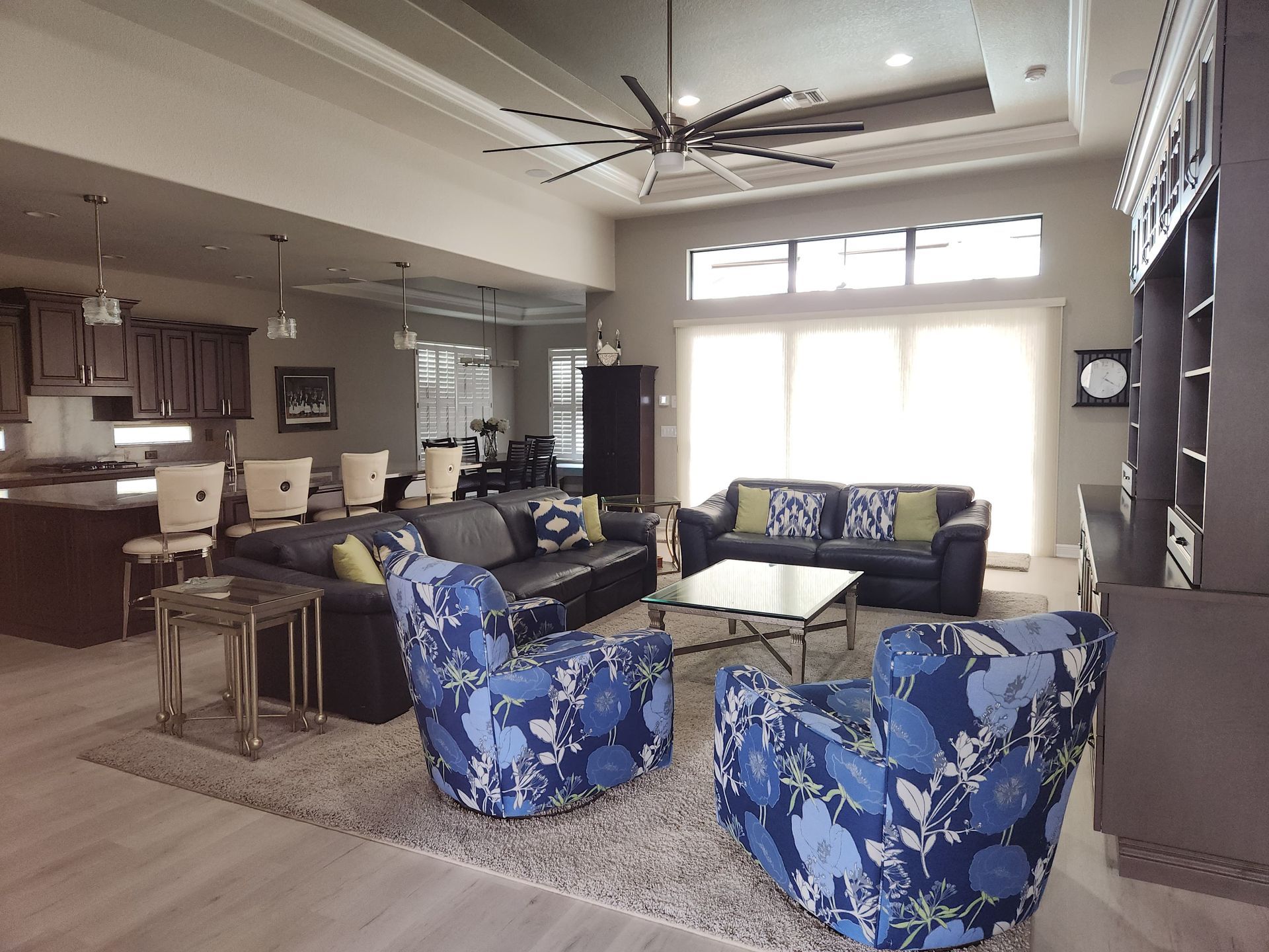 Four people cleaning a kitchen: wiping surfaces, mopping floor. Light-filled room with white cabinets, appliances.