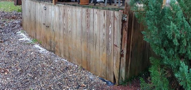 A weathered wooden deck skirt wall installed outdoors next to mulch and a green bush.