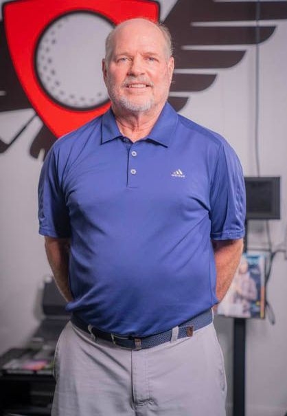 A man in a blue shirt and gray pants is standing in front of a wall with a golf ball on it.