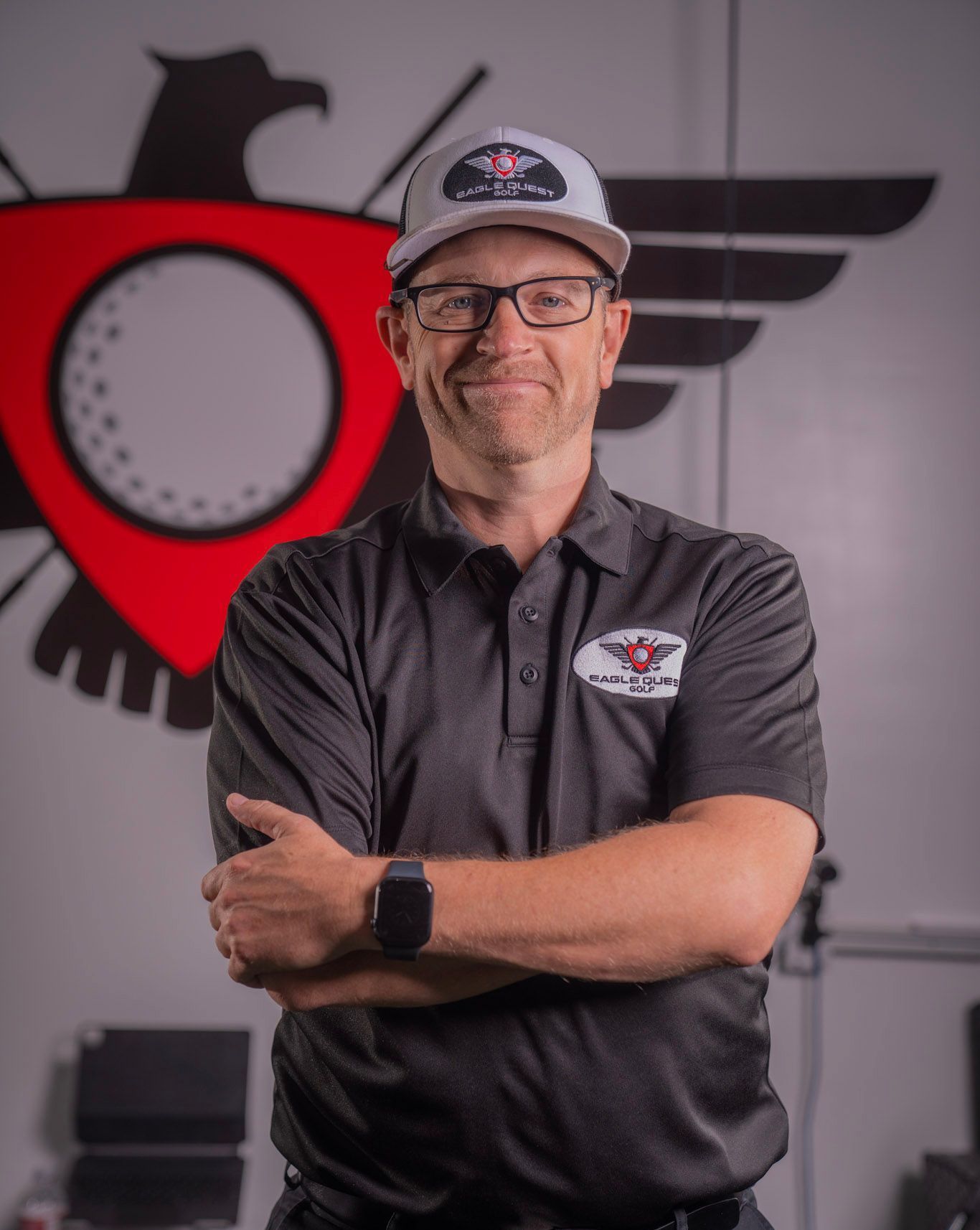 A man wearing glasses and a hat is standing with his arms crossed