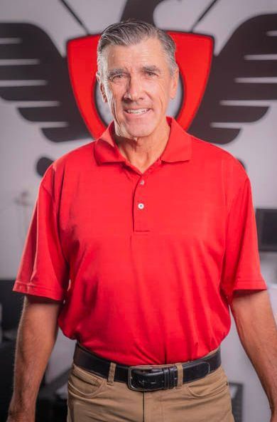 A man is wearing a red polo shirt and khaki pants.