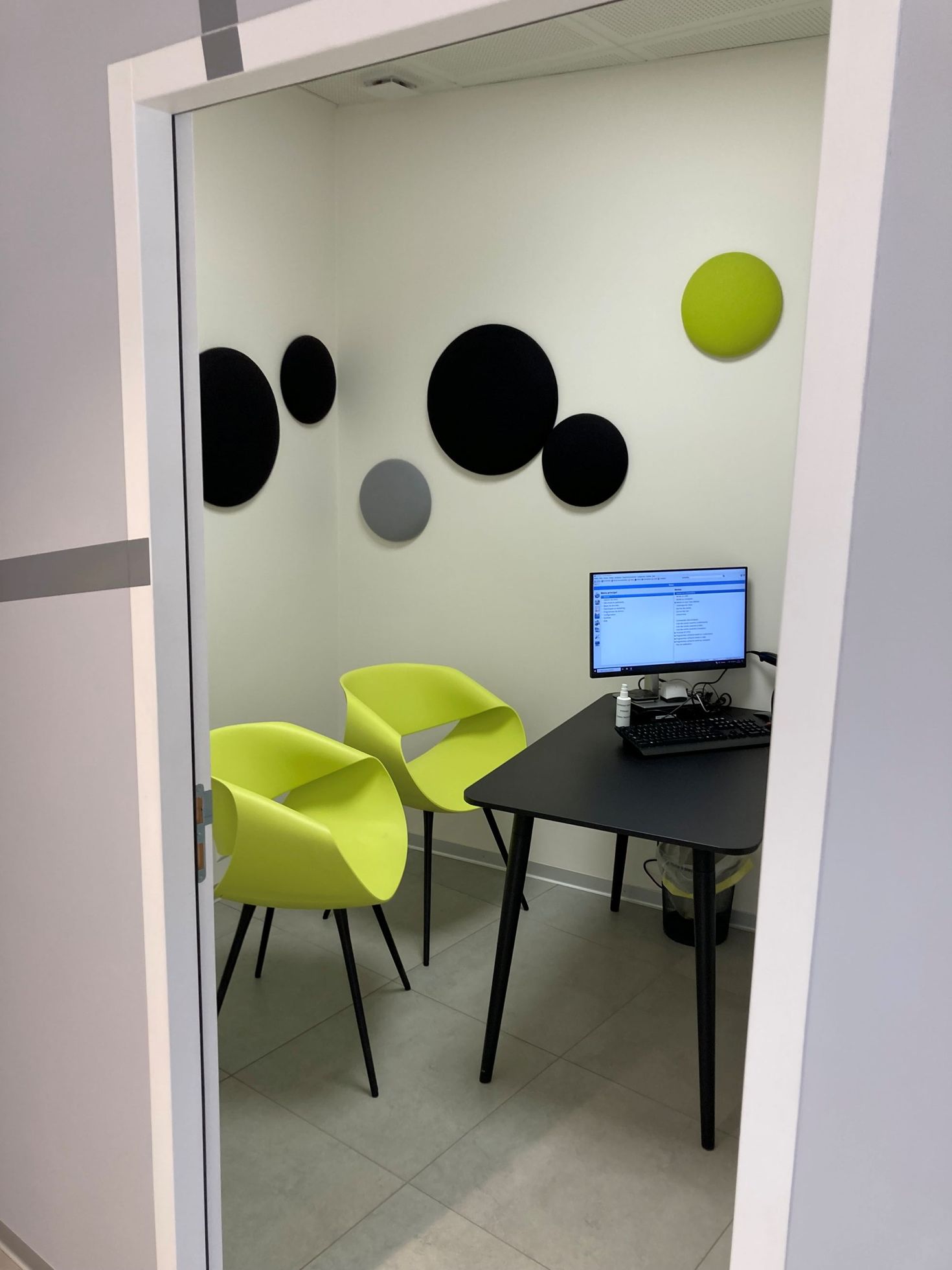 Ein kleines Büro mit zwei hellgrünen Stühlen, einem schwarzen Schreibtisch mit Computer und runden Akustikwandpaneelen.