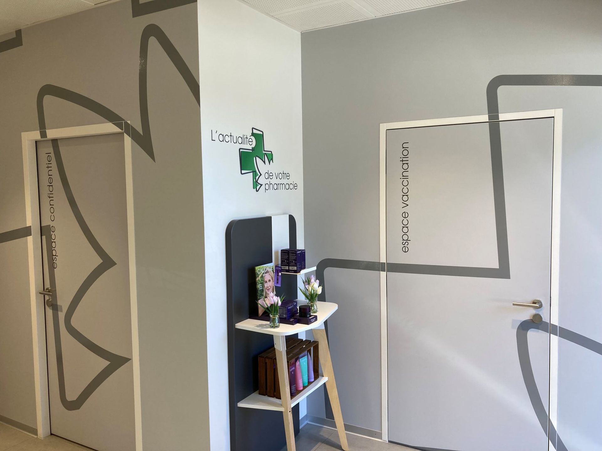 Eine Ecke in einem Arztzimmer mit zwei Türen, grauen Wänden mit grauen Linienzeichnungen und einem kleinen Ausstellungsregal.