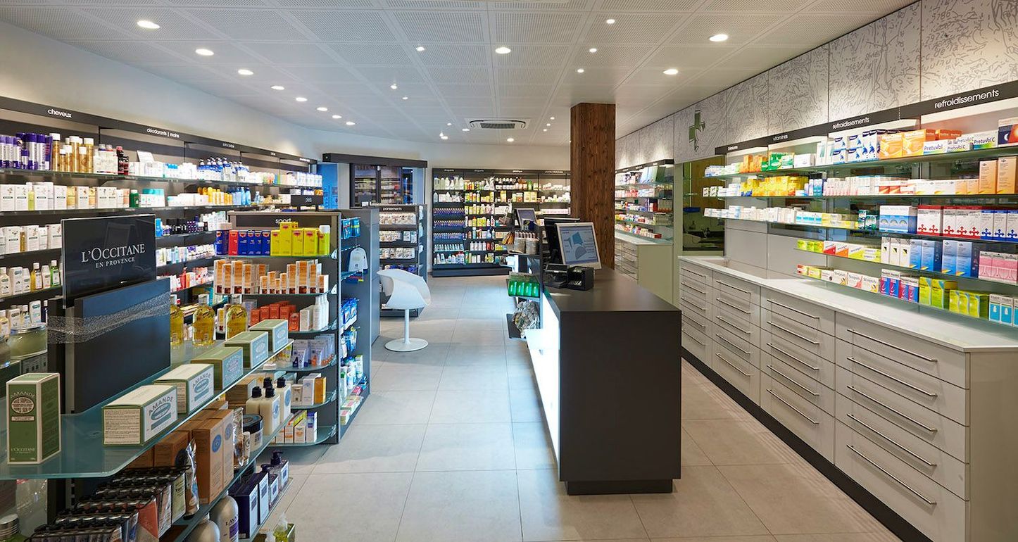 Intérieur d'une pharmacie éclairé et organisé, étagères blanches, divers produits de santé et un comptoir de caisse central.