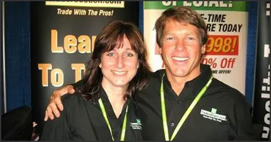 A man and a woman are posing in front of a sign that says trade with the pros
