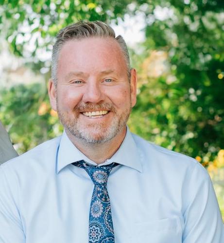 A smiling person wearing a light blue button-down shirt