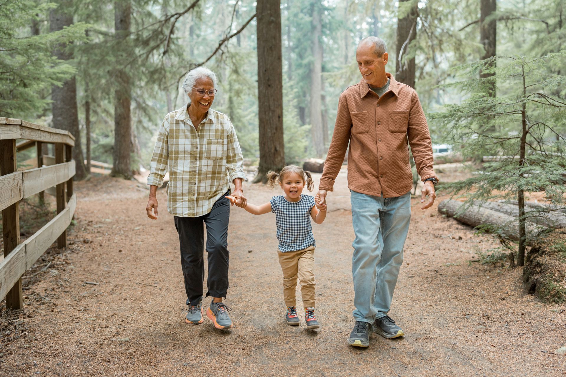Two adults and a child walking hand-in-hand along a dirt path in a forest.