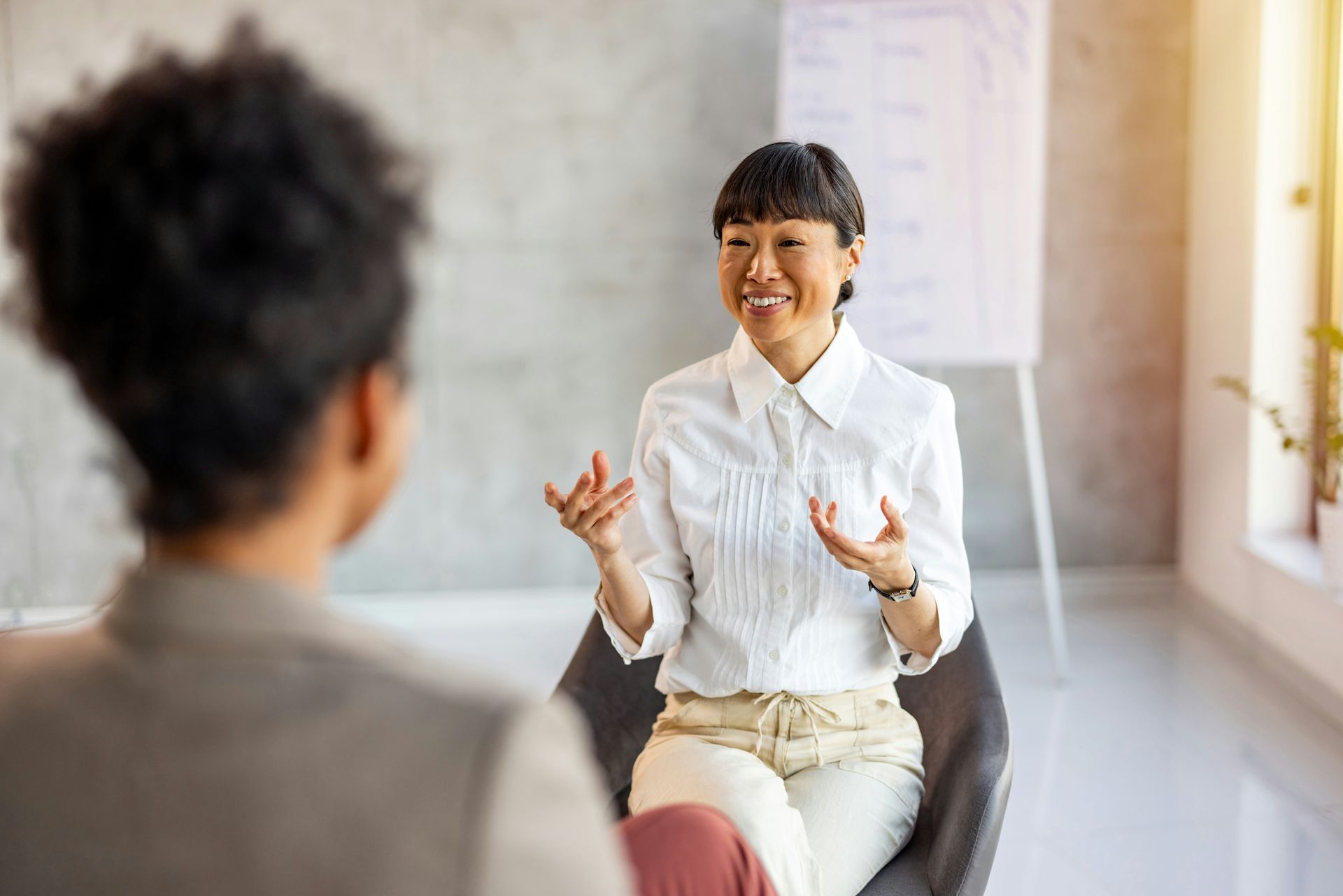 Two colleagues seated in a modern office, one speaking with expressive gestures, the other seen from the back.